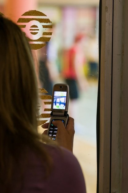 A close-up shot of a person using a smartphone to make a contactless payment at a retail checkout. The focus is on the phone and the payment terminal, with a blurred background showing other shoppers. The image emphasizes ease and convenience.