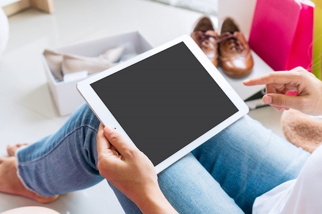 Close-up shot of a woman's hands using a tablet to browse the Shein website. A wishlist with various clothing items is visible on the screen.
