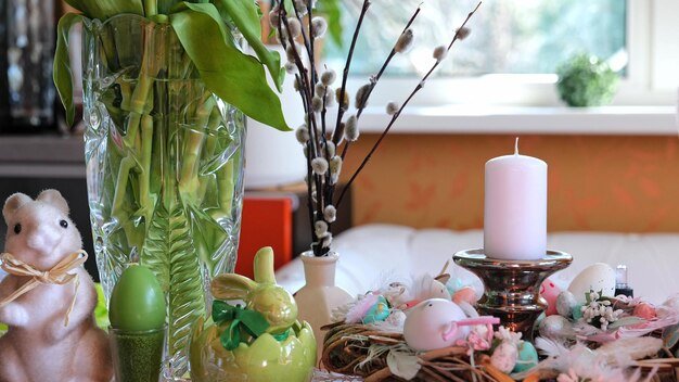 A close-up shot of a DIY Easter garland made from colorful felt scraps and cotton balls. The garland is strung across a mantelpiece decorated with small, potted spring flowers.