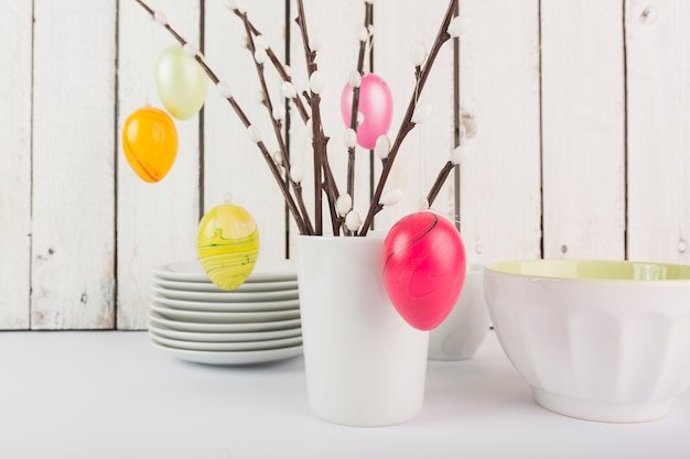 An Easter table centerpiece featuring a rustic wooden basket brimming with colorful Easter eggs, spring flowers like tulips and daffodils, and greenery. The basket is surrounded by scattered pastel-colored eggs, creating a charming and festive Easter display.