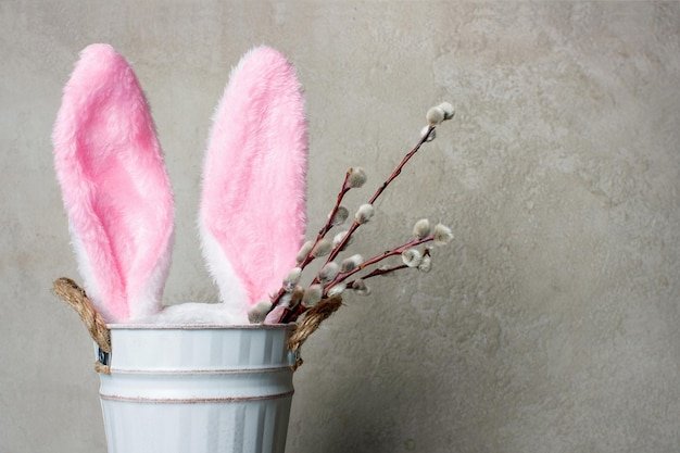 A close-up of an Easter table setting featuring pastel-colored plates (light green, blush pink, pale yellow), gold cutlery, and linen napkins tied with baby blue ribbon. Decorative pastel eggs are scattered around the centerpiece of pastel-colored flowers. The light is soft and diffused, highlighting the delicate colors and textures.
