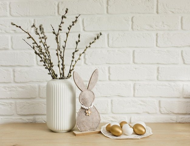 A close up image of two white candles on a wooden table, surrounded by small glass vases with single white flowers in each. Beside the candles are two bunny shaped decorations made of wood and painted white.