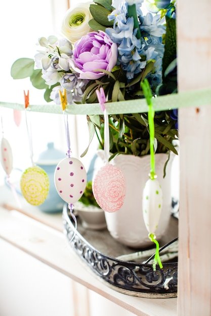 A close-up shot of a colorful Easter egg garland made from felt scraps and yarn, strung across a rustic wooden mantelpiece. The garland features various shapes and sizes of eggs, each adorned with unique embroidery and beadwork.