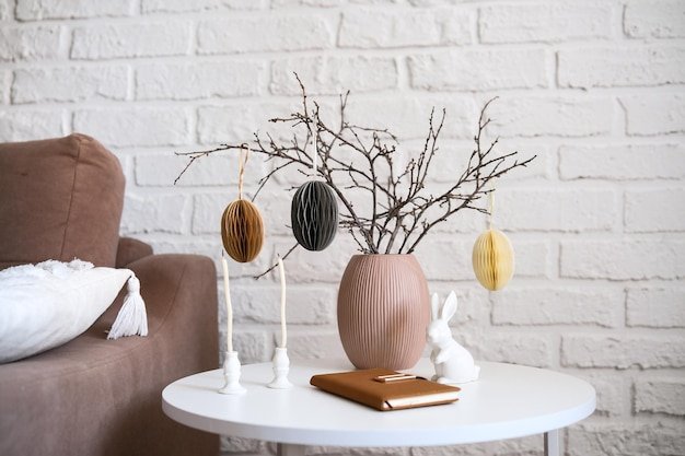 A close-up shot of a rustic wooden table centerpiece featuring a bird's nest filled with pastel-colored eggs and adorned with delicate feathers. The nest is surrounded by moss and small spring flowers, showcasing a natural and handcrafted Easter decoration.